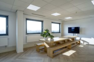 Kantoorruimte aan de Joan Muyskenweg met grote houten vergadertafel, planten, muurtelevisie en veel daglicht.